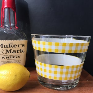 May include: A glass with a yellow and white checkered pattern, a bottle of Maker's Mark whiskey, and a lemon.
