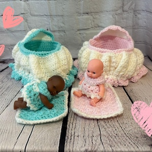 May include: Two handmade crochet baby cradles, one blue and white, the other pink and white, each with a small doll. The cradles have a ruffled design. The dolls are wearing matching crochet outfits and resting on small blankets.
