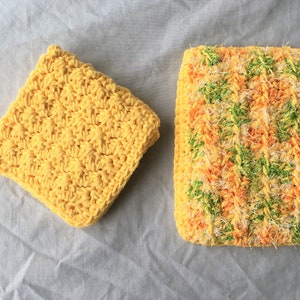 Op de afbeelding: Twee gebreide theedoeken, een gele en een met gele, oranje en groene strepen.