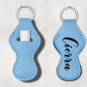May include: Two blue keychains with a white geometric pattern. One keychain has a slot for a lip balm and the other keychain has the name "Ciara" written in black cursive.