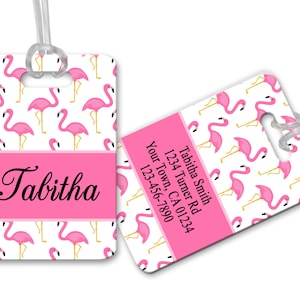 May include: Pink flamingo luggage tag with a white background and a pink stripe with the name Tabitha. The tag has a clear plastic strap for attaching to luggage. The back of the tag has a pink background with white text that reads: Tabitha Smith, 1234 Turner Rd, Your Town, CA 01234, 123-456-7890.