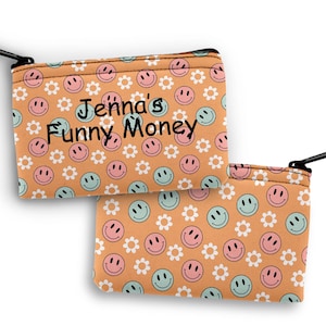 May include: A small orange zippered pouch with a repeating pattern of pink and green smiley faces and white flowers. The pouch has the text "Jenna's Funny Money" printed on the front.