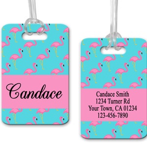 May include: Two luggage tags with a flamingo pattern on a turquoise background. One tag has the name "Candace" in cursive, the other has contact information. Both tags have a pink stripe at the bottom and a clear plastic loop.