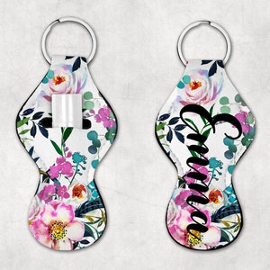 May include: A white floral patterned keychain with a black zippered pocket for lip balm or a small tube of hand sanitizer. The keychain has a black metal ring and the name "Emma" is printed in black on the front.