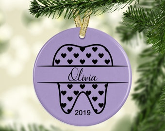 May include: Purple ceramic Christmas ornament shaped like a tooth with black hearts and the name Olivia and the year 2019.