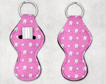 May include: Pink key chain with a lip balm holder. The key chain is decorated with a repeating pattern of white teeth with red jump ropes.