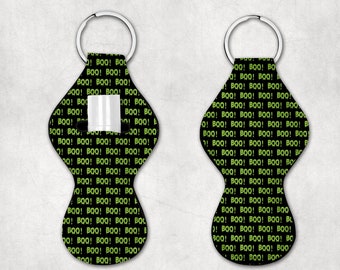 May include: A black and green key chain with a repeating pattern of the word "BOO!" in green. The key chain has a small pocket for a lip balm or other small item.
