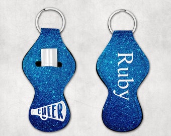 May include: Two blue glitter keychain holders with a silver key ring. One holder has a white megaphone with the word "CHEER" on it. The other holder has the name "Ruby" written in white.
