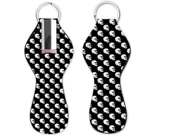 May include: Black key chain with a white skull pattern. The key chain has a metal ring and a slot for a small item, such as a lipstick or a key.