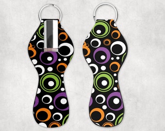 May include: A black, white, green, and purple circle patterned key chain with a clear plastic bottle holder. The key chain is designed to hold a small bottle of nail polish.