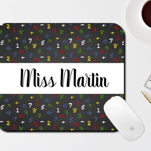 May include: Black mouse pad with a white border and a repeating pattern of colorful math equations on a black background. The text "Miss Martin" is printed in black on a white banner across the middle of the mouse pad.