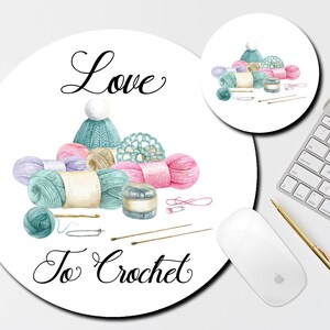 May include: A round mousepad with a watercolor illustration of yarn, crochet hooks, and a hat. The text "Love to Crochet" is written in black cursive font.