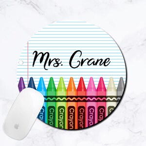 K&ouml;nnte beinhalten: Eine runde Mauspad mit einem blau-wei&szlig; gestreiften Hintergrund. Der Text "Mrs. Crane" ist oben auf der Mauspad in Schwarz gedruckt. Eine Reihe bunter Stifte ist unten auf der Mauspad gedruckt.