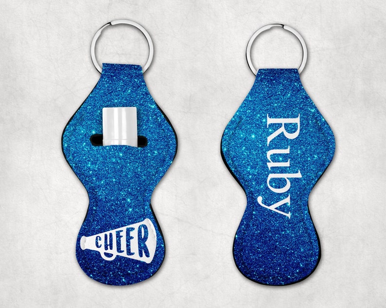 Peut inclure: Deux porte-cl&eacute;s en paillettes bleues avec un anneau de cl&eacute; argent&eacute;. Un porte-cl&eacute;s a un m&eacute;gaphone blanc avec le mot "CHEER" dessus. L'autre porte-cl&eacute;s a le nom "Ruby" &eacute;crit en blanc.