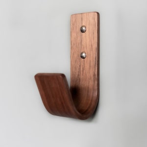 May include: A wooden wall hook with a curved design. The hook is made of dark brown wood and has two silver screws.