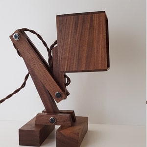 K&ouml;nnte beinhalten: Eine Schreibtischlampe aus Holz mit einem quadratischen Schirm und einem Gelenkarm. Die Lampe ist aus dunkelbraunem Holz gefertigt und hat ein schwarzes Kabel.