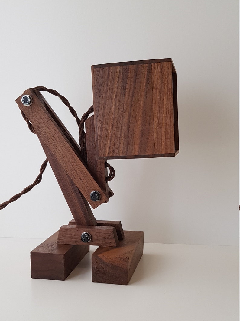 K&ouml;nnte beinhalten: Eine Schreibtischlampe aus Holz mit einem quadratischen Schirm und einem Gelenkarm. Die Lampe ist aus dunkelbraunem Holz gefertigt und hat ein schwarzes Kabel.