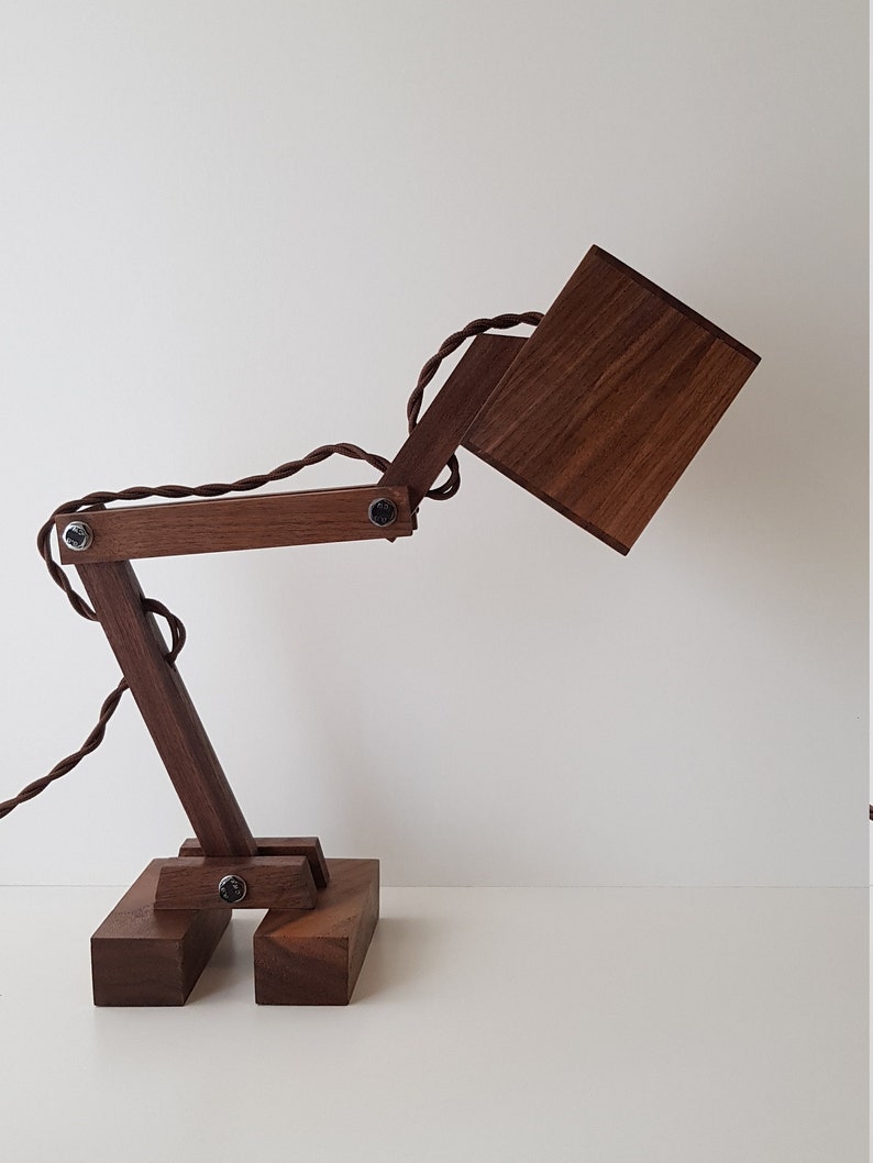 K&ouml;nnte beinhalten: Eine Schreibtischlampe aus Holz mit brauner Oberfl&auml;che. Die Lampe hat einen quadratischen Schirm und einen flexiblen Arm, der in verschiedene Positionen eingestellt werden kann.