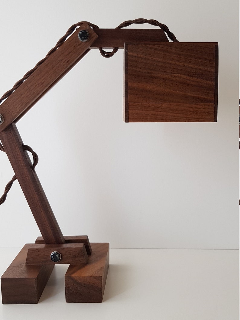 K&ouml;nnte beinhalten: Eine Schreibtischlampe aus Holz mit brauner Oberfl&auml;che. Die Lampe hat einen langen, beweglichen Arm und einen quadratischen Schirm. Die Lampe ist aus massivem Holz gefertigt und hat ein schlichtes, modernes Design.