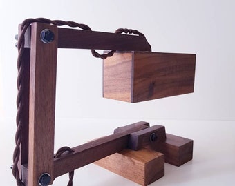 Könnte beinhalten: Eine Schreibtischlampe aus Holz mit einem braunen Kabel und einem rechteckigen Schirm. Die Lampe ist aus dunklem Holz gefertigt und hat ein schlichtes, industrielles Design.