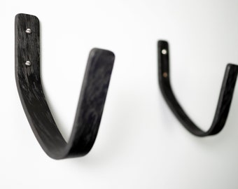 Puede incluir: Dos ganchos de pared de madera negra con un diseño curvo. Los ganchos están montados en una pared blanca.