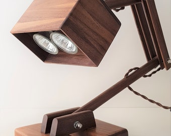 Könnte beinhalten: Eine Schreibtischlampe aus Holz mit einem rechteckigen Schirm und zwei Glühbirnen. Die Lampe hat einen braunen Holzfuß und einen langen, verstellbaren Arm.