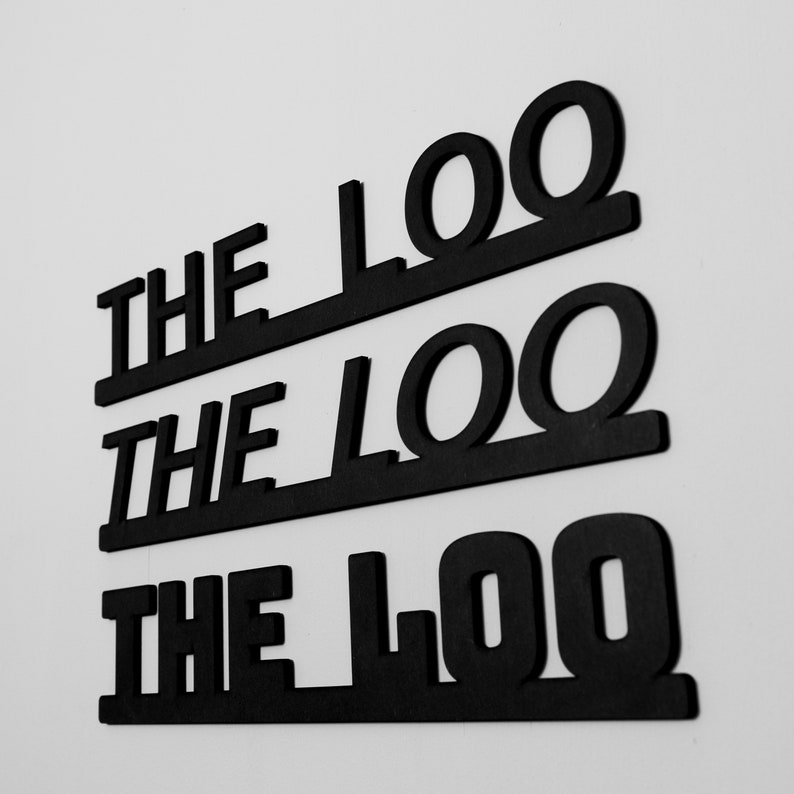 Black 'The Loo' Text Word Sign by NOIR. DESIGN for Hallway or Bathroom Décor showcasing all 3 fonts - thick bold - Medium Bold and italic stuck on the wall with adhesive tabs