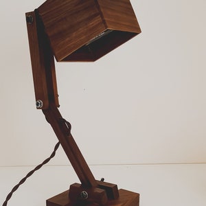 K&ouml;nnte beinhalten: Eine Schreibtischlampe aus Holz mit einem quadratischen Schirm und einem Gelenkarm. Die Lampe ist aus dunkelbraunem Holz gefertigt und hat ein schwarzes Kabel.