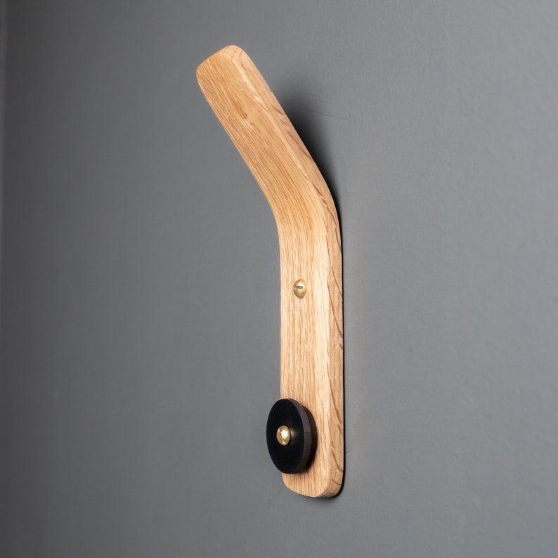 A functional and versatile oak wood wall hook with a black leather accent, perfect for hanging coats, hats, bags, and keys near the entrance