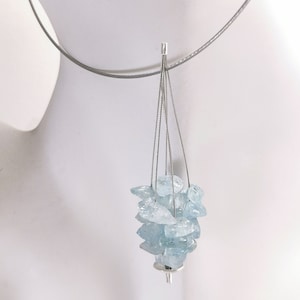 May include: A contemporary necklace with a cascade of pale blue aquamarine stones, each with an irregular shape, held by fine silver wires. The necklace is suspended from a silver-toned cable, offering a minimalist aesthetic. The stones are grouped, forming a distinctive centrepiece.