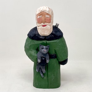 May include: A hand-carved wooden figurine of Santa Claus wearing a green coat with a black fur collar. He is holding a gray cat in his arms and a small gray mouse is perched on his shoulder.