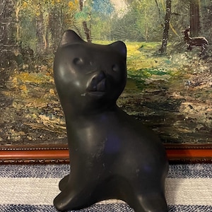 May include: A black ceramic cat figurine with a stylized design. The cat is sitting with its head turned to the side and its mouth slightly open.