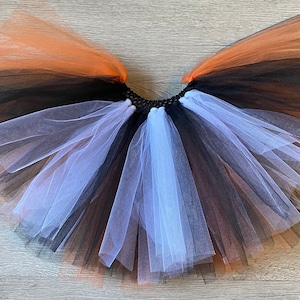 Könnte beinhalten: Ein mehrlagiger Tüllrock in Orange, Schwarz und Weiß. Der Rock besteht aus weichem, fließendem Tüll und hat einen elastischen Bund.