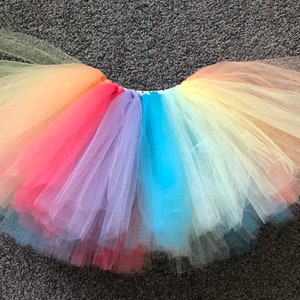 May include: A rainbow tulle tutu skirt with layers of yellow, orange, red, pink, purple, blue, and light blue tulle.
