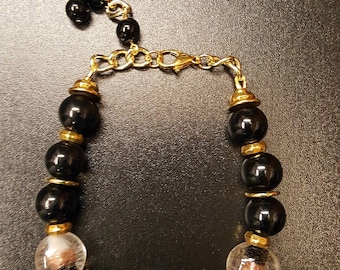May include: A black and gold beaded bracelet with a clear crystal charm. The bracelet has a gold chain clasp.