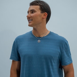 May include: A man wearing a blue striped t-shirt with a silver chain necklace and a tree pendant.