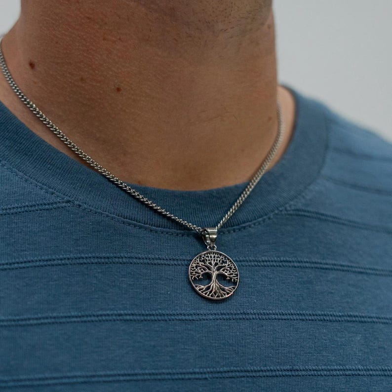 May include: A silver chain necklace with a tree of life pendant. The pendant is round and features a detailed design of a tree with branches and leaves.