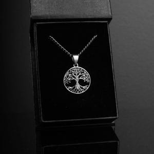 May include: A silver necklace with a tree of life pendant. The pendant is a circular design with a detailed tree with branches and roots.