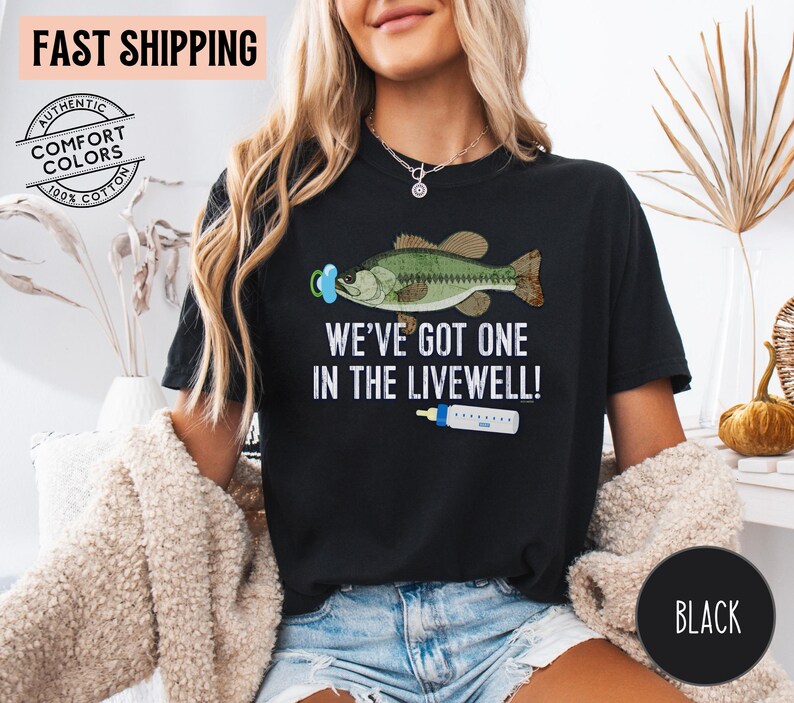 May include: Black t-shirt with the text "WE'VE GOT ONE IN THE LIVEWELL!" featuring a cartoon bass wearing a pacifier and a baby bottle. The shirt is made of 100% cotton.