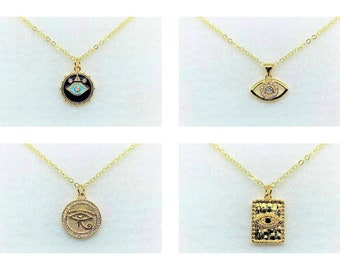 May include: Four gold-colored necklaces with pendants featuring eye designs. The pendants include a circular pendant with a black background and a turquoise eye, an eye-shaped pendant with a crystal center, a circular pendant with an eye symbol, and a rectangular pendant with an eye design.