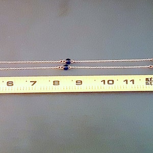 May include: A silver chain necklace featuring blue and white evil eye beads. The necklace is about 43 cm long, measured with a yellow tape measure. The beads are dark and light blue, with an eye design in the center.