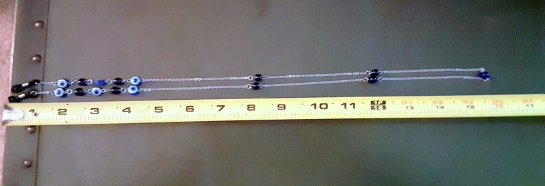 May include: A silver chain eyeglass holder with blue and black beads. The eyeglass holder is approximately 43 cm long.