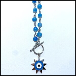 May include: A silver chain necklace with blue glass beads and a silver star charm with a blue evil eye in the center.