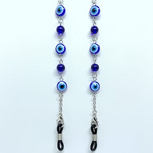 May include: Two eyeglass chains featuring blue and white evil eye beads and dark blue beads. The chains are silver-coloured and have small clasps for attaching to glasses. The background is white.