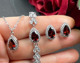 May include: A silver necklace, bracelet, and earrings set with teardrop-shaped red gemstones surrounded by clear cubic zirconia stones.