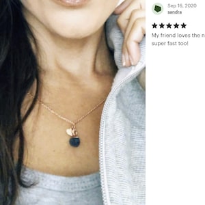 May include: A gold chain necklace with a small heart charm and a larger black lava stone pendant.