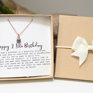 May include: A gift box with a white card that reads "Happy 21st Birthday". The card is inside a brown box with a white bow. The card has a message about looking back at accomplishments and building a beautiful life. The box also contains a necklace with a small blue stone pendant.