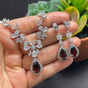 May include: A silver necklace and earrings set with a floral design and teardrop-shaped red stones.