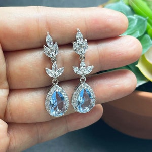 May include: A pair of silver teardrop earrings with a light blue gemstone and clear crystal accents.