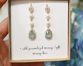May include: A pair of blue aquamarine teardrop earrings with a pearl and crystal design. The earrings are in a small white box with a gold trim. The box has a message that says "add personalized message/gift message here" and "#10 blue aquamarine".